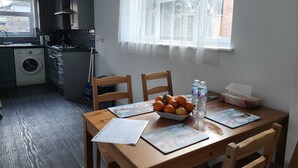 Une cuisine compacte équipée d’un lave-linge, d’une table à manger avec des chaises et d’une fenêtre agrémentée de rideaux en dentelle.