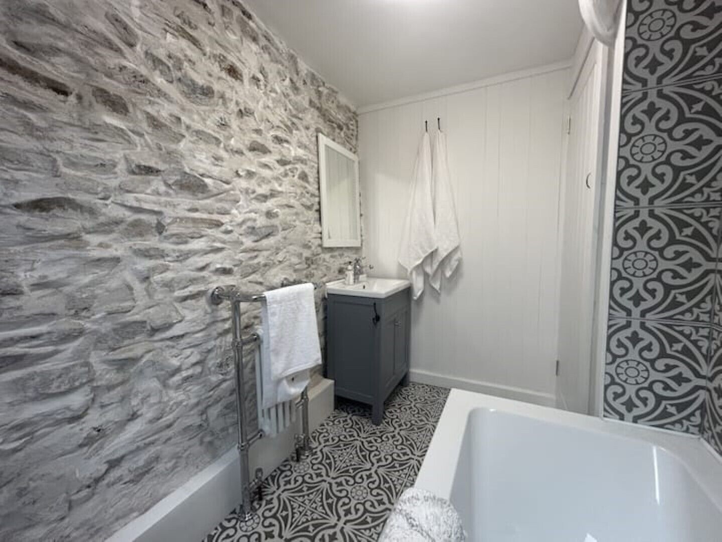 Un baño con pared de piedra, lavamanos, espejo y bañera.