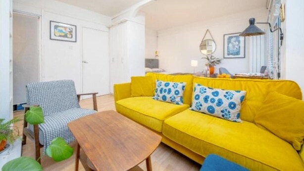 Een lichte woonkamer met een geel bankje, een geruite stoel en een houten tafel.