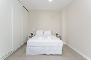 Un lit bien fait, avec du linge de lit blanc et une couvre-lit matelassé, deux tables de chevet avec des lampes et un mur sobre.