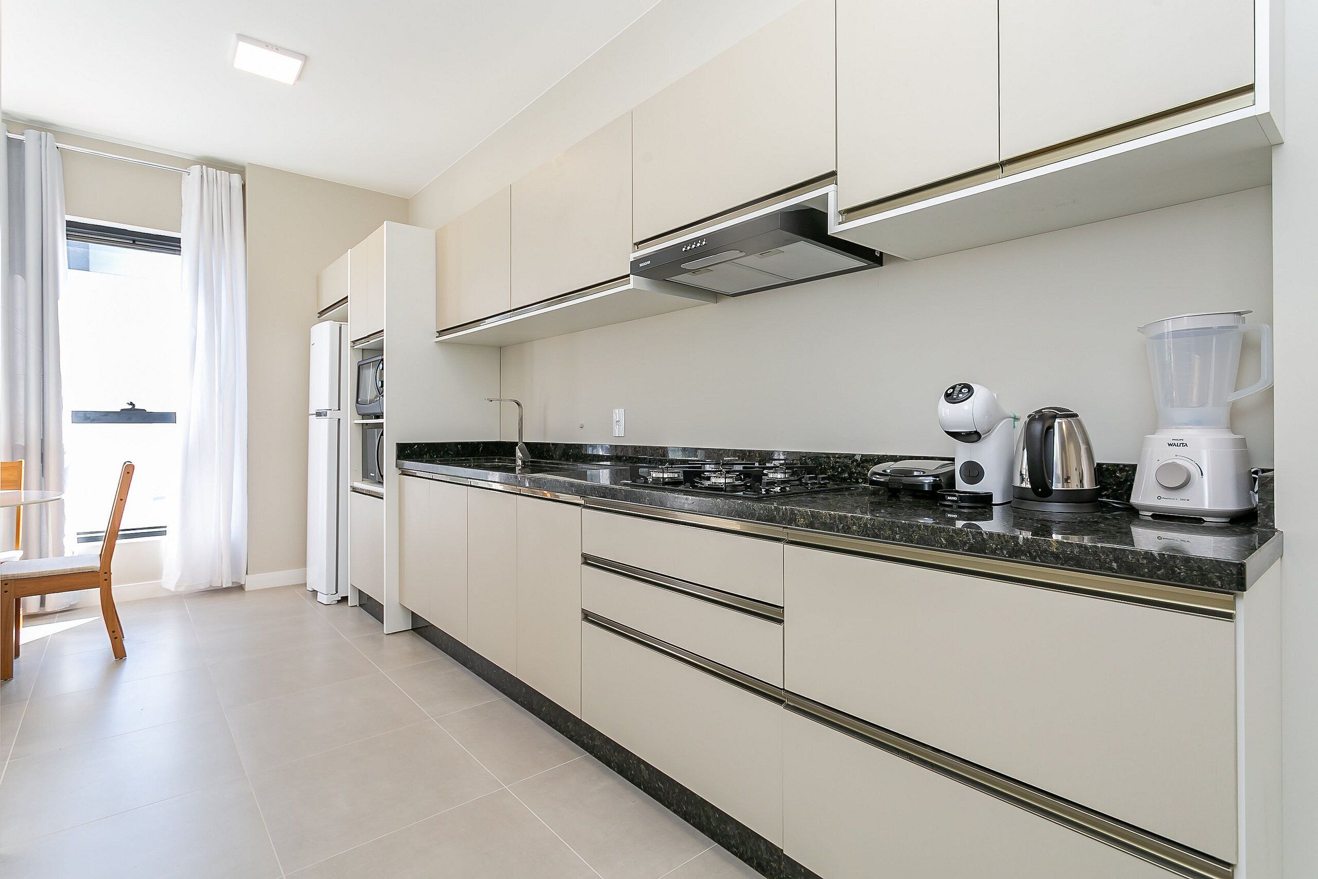 A modern kitchen with white cabinets, a granite countertop, and stainless steel appliances including a refrigerator, microwave, and coffee maker.
