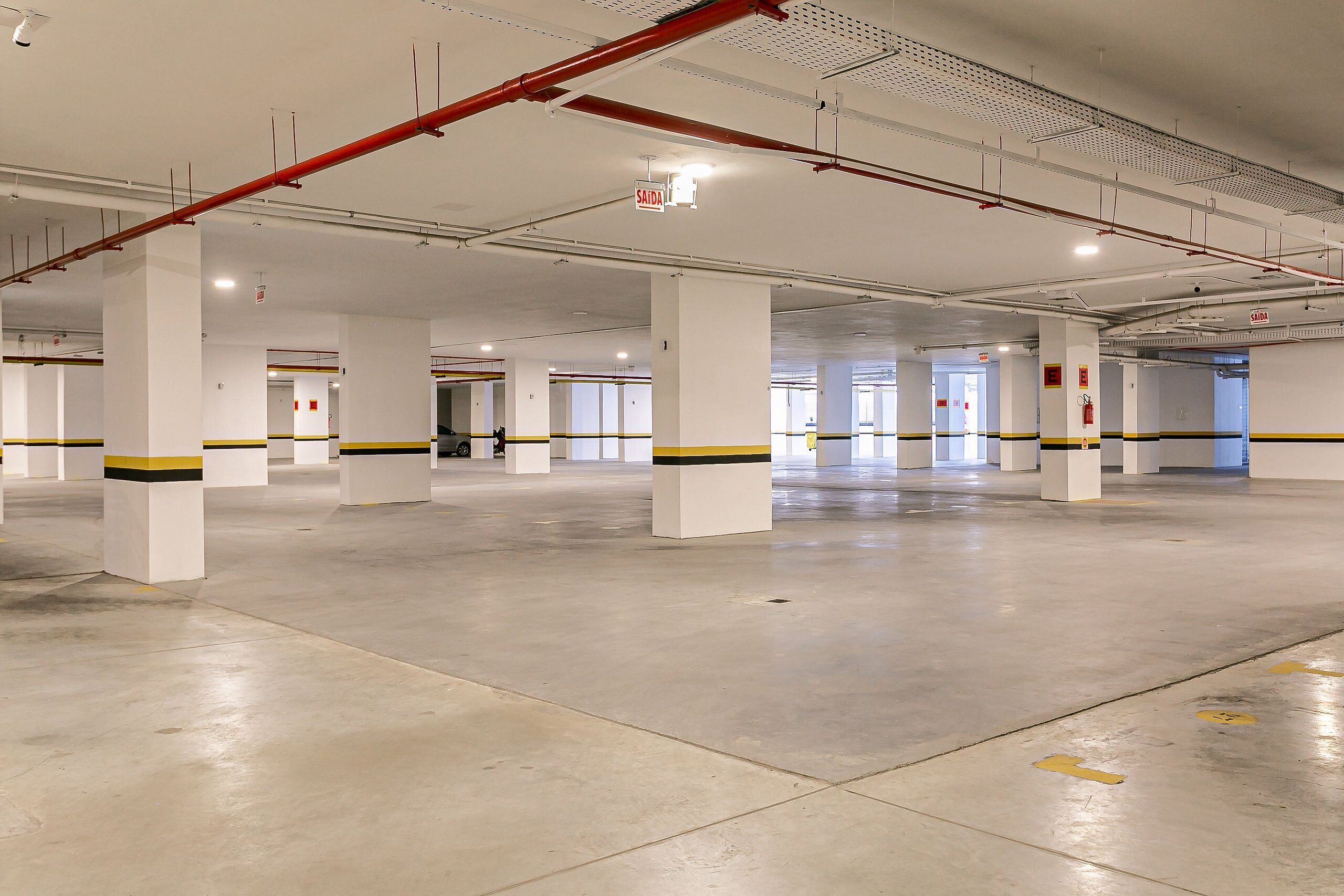 A spacious indoor parking area with white pillars, yellow and black stripes, and red fire safety equipment.