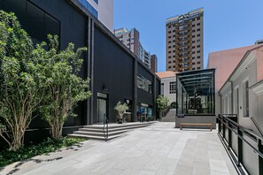 Un edificio moderno con fachada de vidrio, una escalera que conduce a un nivel superior y un banco en primer plano.