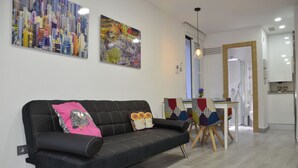 Una sala de estar moderna con un sofá negro, cojines coloridos y dos cuadros abstractos en la pared.