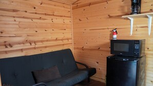 Ein Holzblockhaus-Innenraum mit einer schwarzen Couch, einem schwarzen Kühlschrank und einem Regal mit Kaffeemaschine und Feuerlöscher.