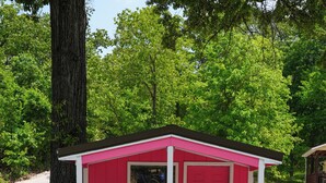 Eine kleine rosa Holzhütte mit Tür, Fenster und einer Bank davor.