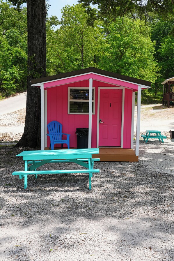 A small pink cabin with a door, a window, and a bench in front.