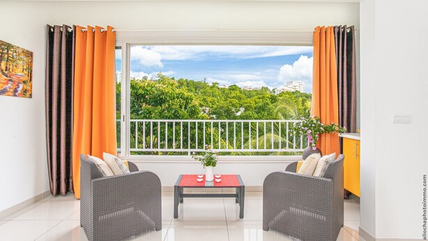A modern living room with a balcony, wicker furniture, a red table, and orange curtains.