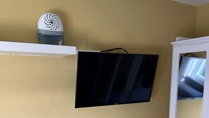 A room with a mounted flat-screen TV, a white cabinet with a mirror, and a small shelf with a decorative item. - Modern One Bedroom Chalet With Central Heating (Bridlington)
