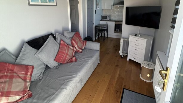 A living room with a sofa, a TV, a kitchen area, and a small dining table. - Modern One Bedroom Chalet With Central Heating (Bridlington)