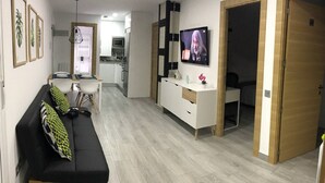 Una sala de estar moderna con un sofá negro, un comedor, una cocina y un televisor en la pared.