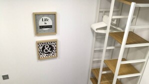 Pared blanca con dos cuadros enmarcados, un estante blanco con repisas de madera y enchufes.