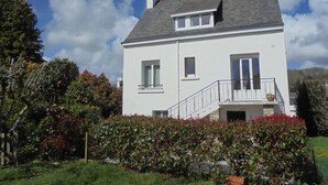 A two-story house with a white exterior, a grey roof, and a small balcony.