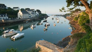 A coastal town with a harbor filled with boats, a lighthouse, and historic buildings along the waterfront.