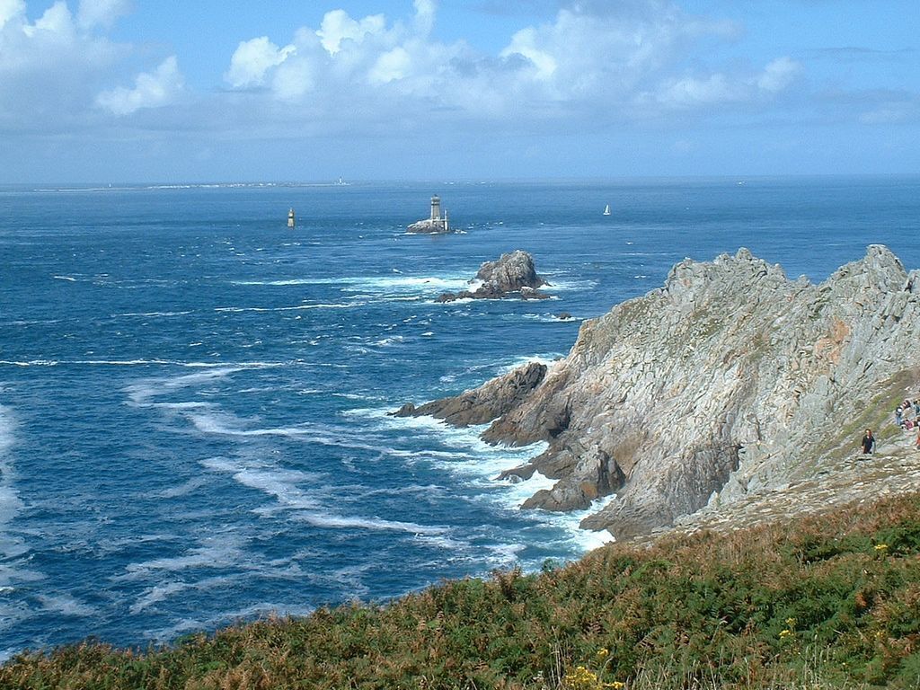 A coastal landscape with rocky cliffs, a lighthouse, and the ocean.