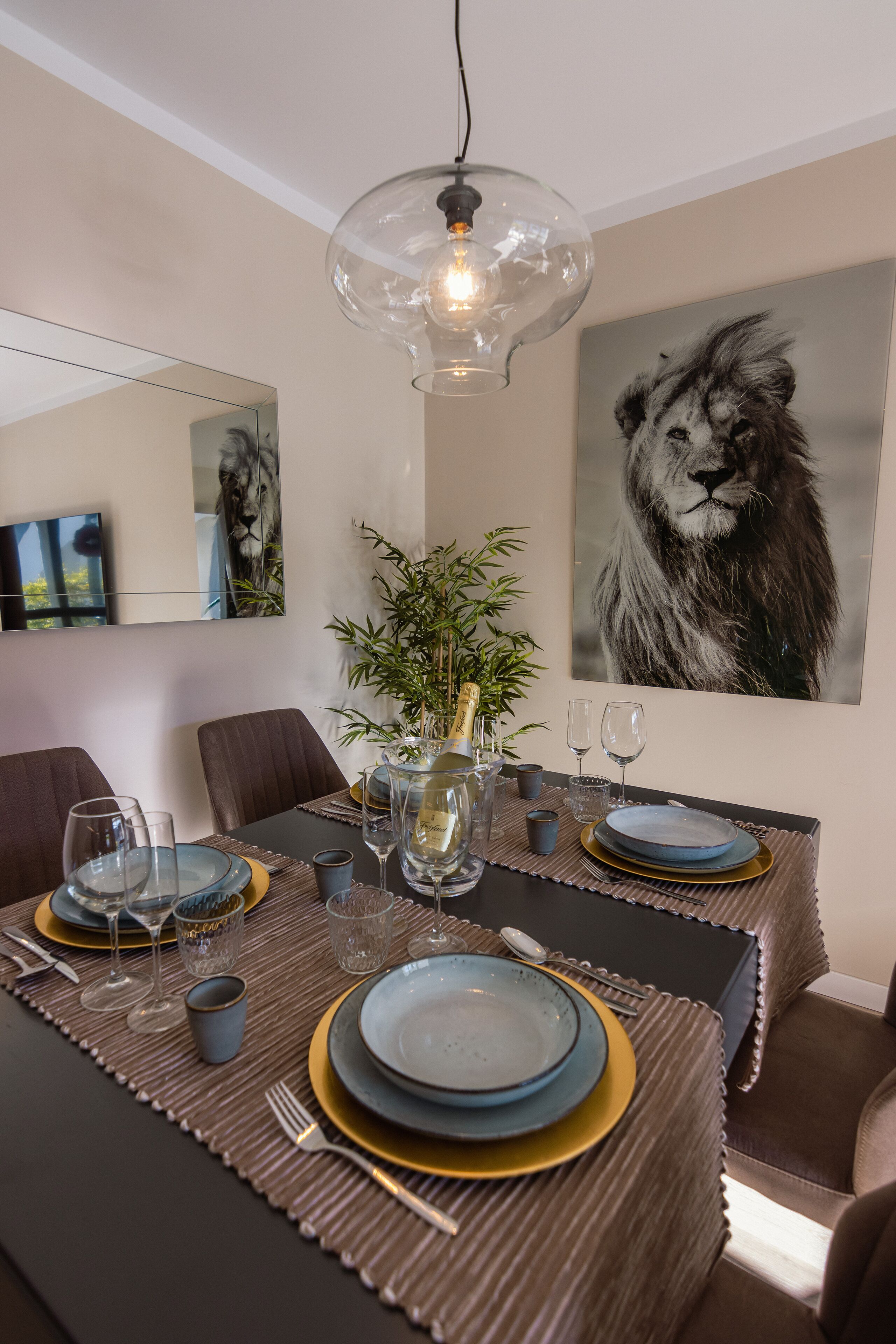 A dining table set with plates, glasses, and cutlery, a vase with flowers, and a framed picture on the wall.