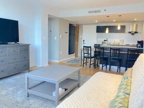 Una sala de estar moderna con un sofá, una mesa de centro, un televisor y una zona de cocina con una mesa de comedor y sillas.