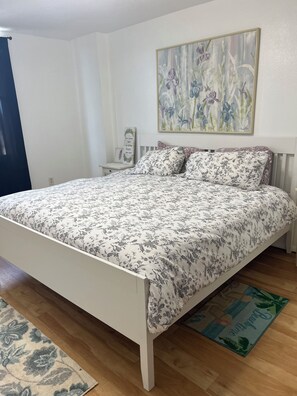 Une chambre à coucher avec un lit, une table de chevet, un tableau accroché au mur et un plancher en bois.