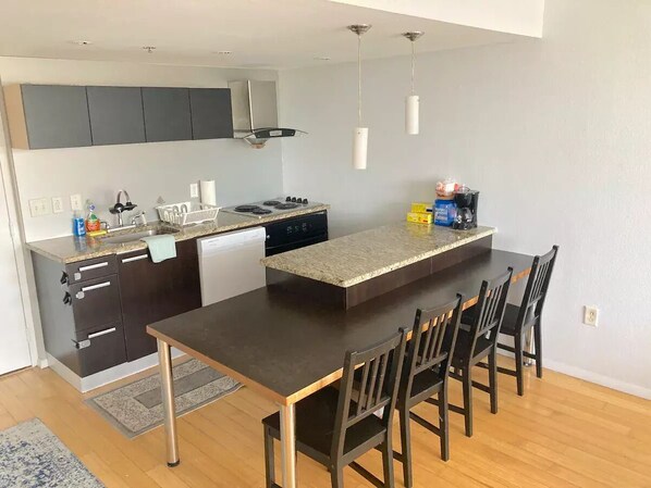Una cocina moderna con una isla central, muebles oscuros y una zona de comedor con cuatro sillas.