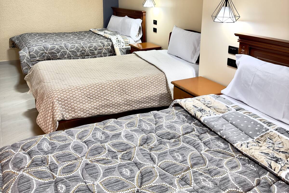A hotel room with two beds, a wooden headboard, a nightstand, and a pendant light.
