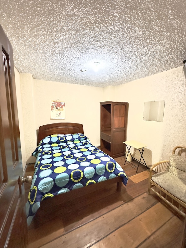 A bedroom with a bed, a wooden wardrobe, a small table, and a chair. - Hostal Niiza (Quito)