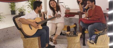 A group of people sitting on wicker chairs in a room with a tiled floor, a hammock, and potted plants.
