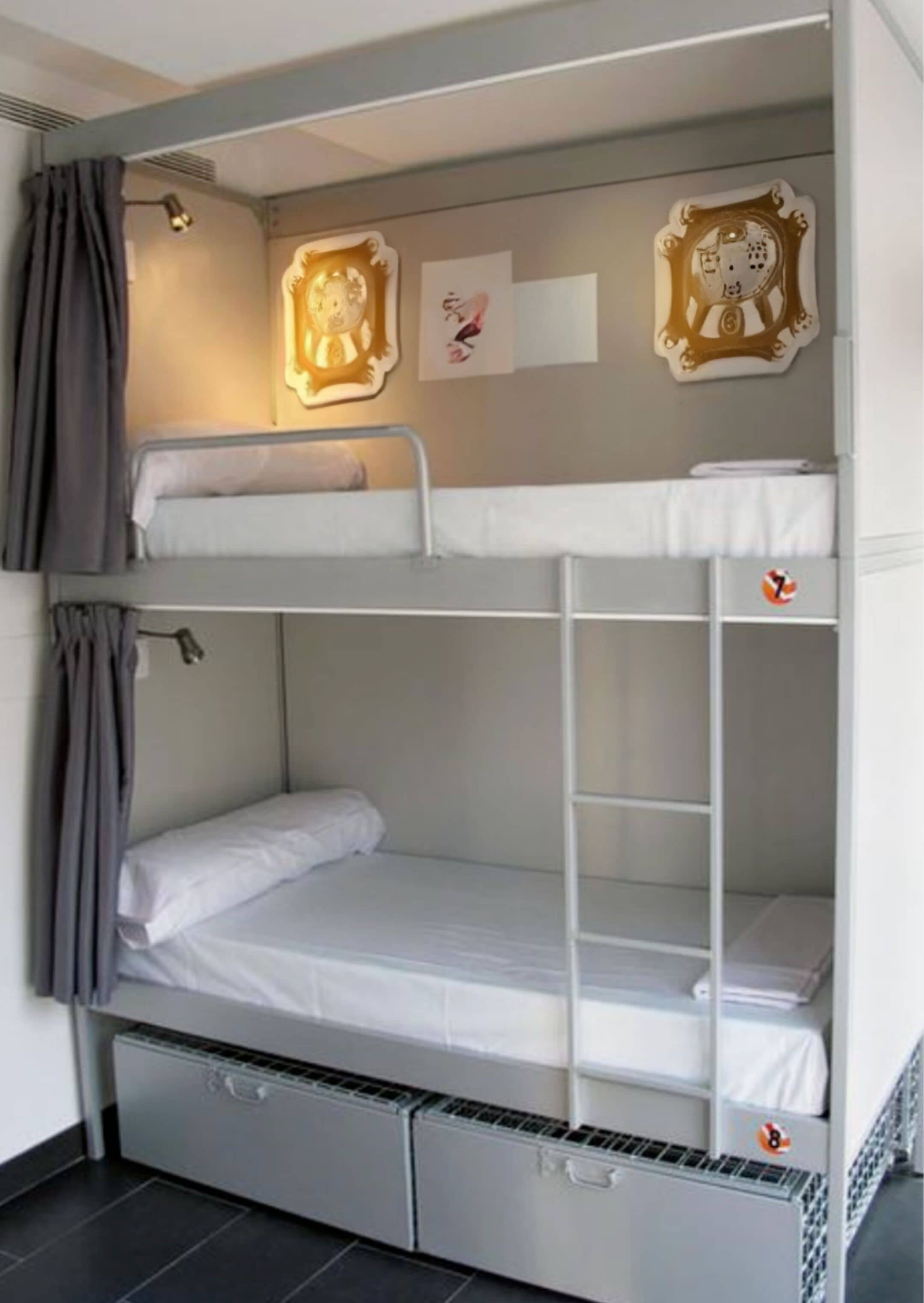 A bunk bed room with a small desk and drawers, a wall-mounted lamp, and two framed pictures.