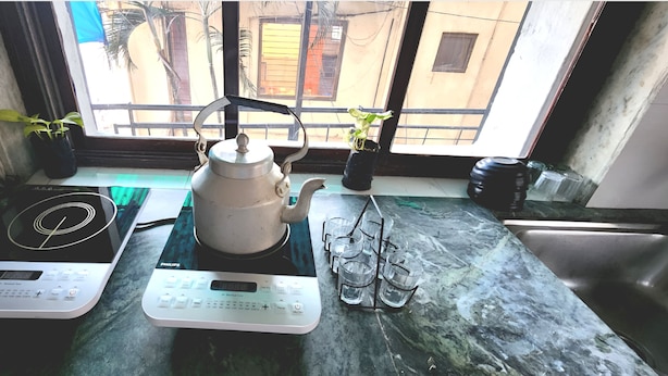 Una encimera de cocina con dos placas de inducción, un hervidor y un escurreplatos con varios vasos.
