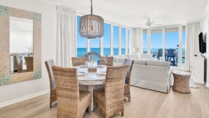 A spacious living room with a dining area, large windows with ocean views, and a modern chandelier. - Colonnades 601 | Beach Front Luxury in Gulf Shores (Gulf Shores)