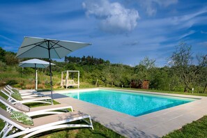 A swimming pool with lounge chairs and a canopy, surrounded by greenery. - Villa Amore, a Romantic Hilltop Farmhouse in Lucca (Lucca)
