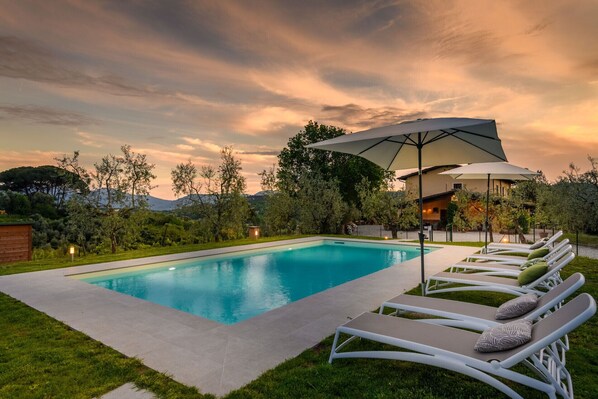 A swimming pool with lounge chairs and umbrellas, surrounded by greenery and a building. - Villa Amore, a Romantic Hilltop Farmhouse in Lucca (Lucca)