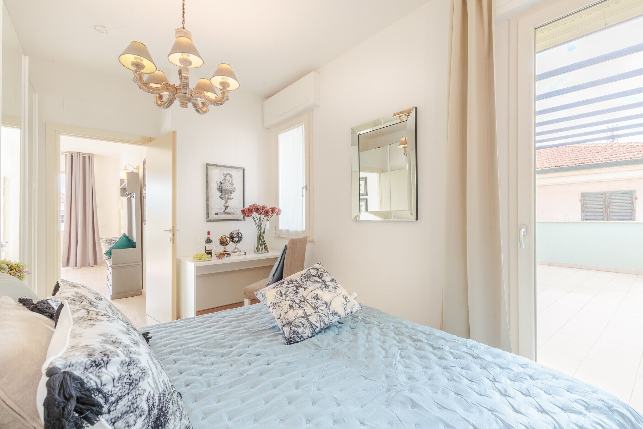 A bedroom with a large bed, a desk, a mirror, and a chandelier.