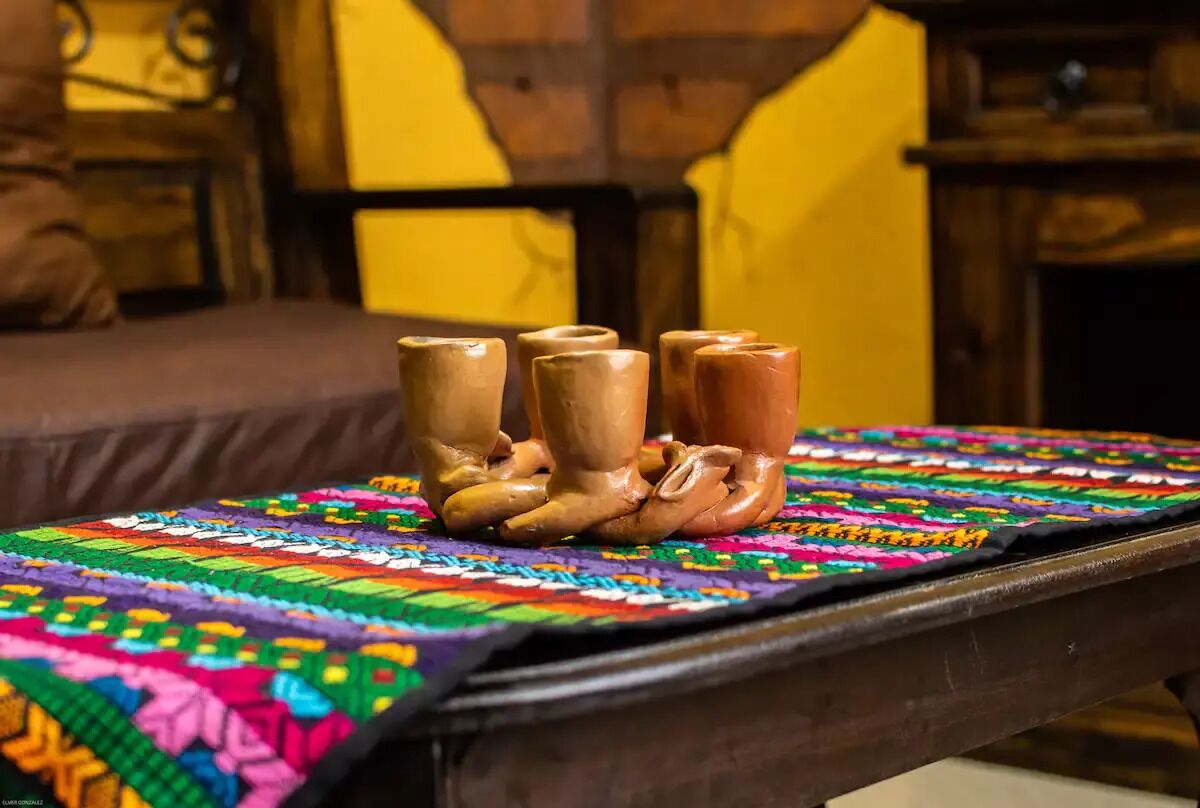 A wooden table with a colorful woven tablecloth and several ceramic objects on it.