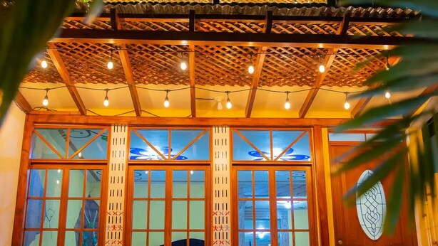 A building with a covered patio area, wooden chairs, and a decorative door.
