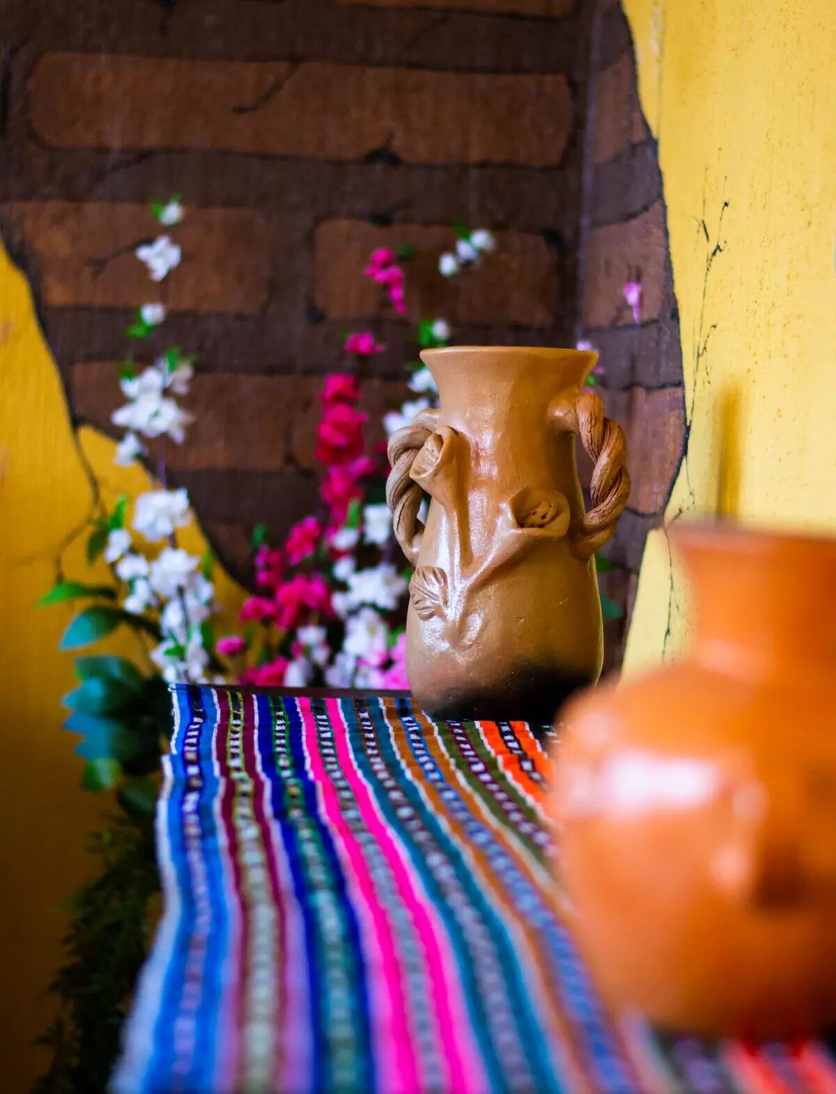 A clay pot with a handle, placed on a colorful woven cloth.