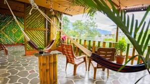 A covered outdoor area with a stone floor, wooden chairs, a hammock, and potted plants.