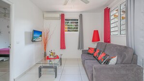 Un salon avec un canapé gris, une table basse en verre, une lampe rouge et un téléviseur fixé au mur.
