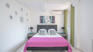 Une chambre à coucher comprenant un lit, deux tables de chevet, un ventilateur de plafond, des œuvres d’art murales et un appareil de climatisation.