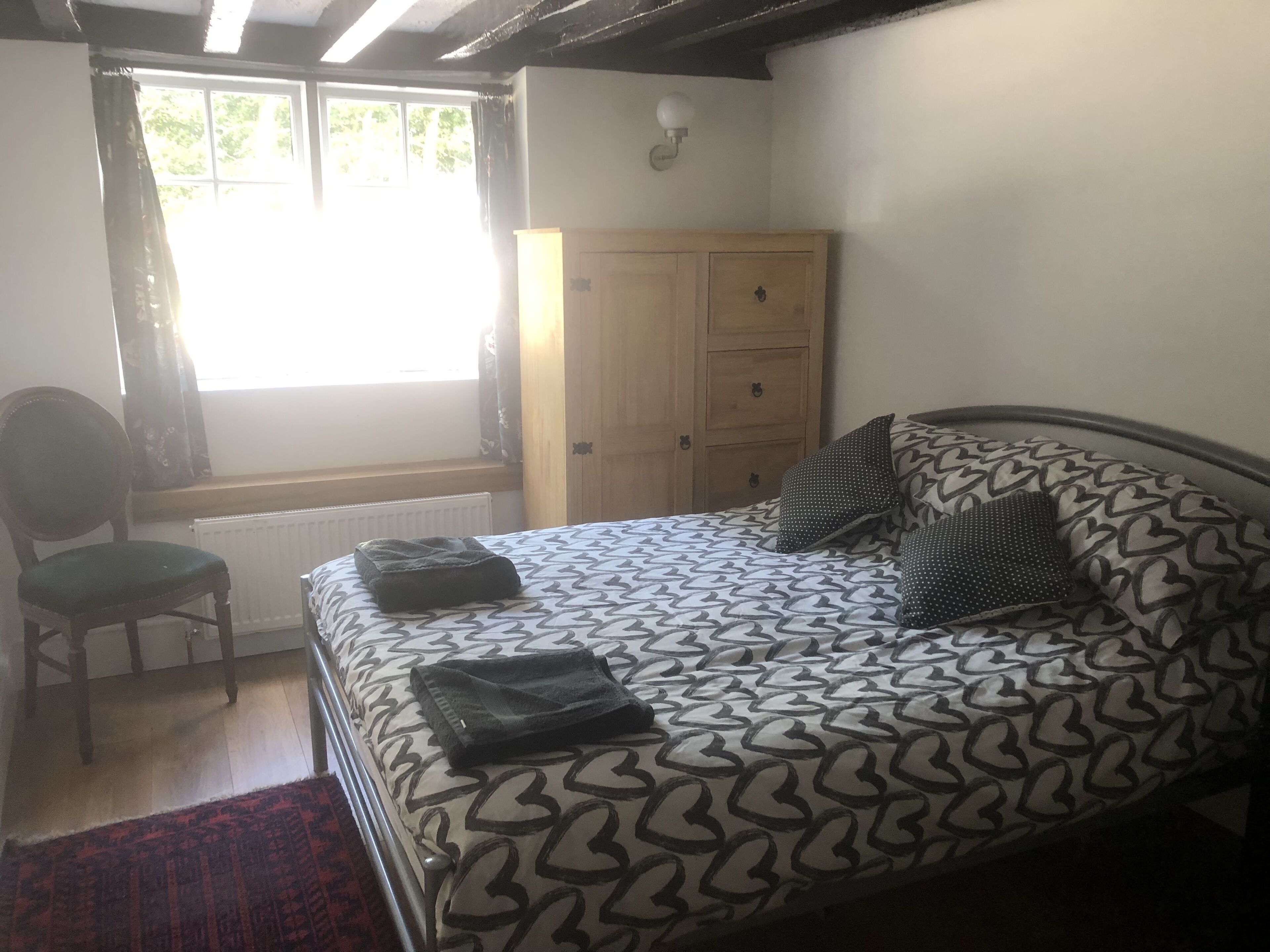 A bedroom with a bed, a chair, a wardrobe, and a window.
