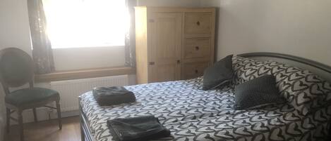 A bedroom with a bed, a chair, a wardrobe, and a window.