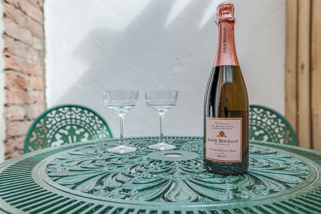 Een fles Louis Bouillot Grand Reserve Rosé Brut op een groene metalen tafel met drie wijnglazen.