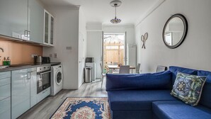 Eine moderne Küche mit Waschmaschine, ein Essbereich mit Tisch und Stühlen sowie ein blaues Sofa mit gemustertem Kissen.
