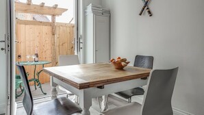 Ein Essbereich mit einem Holztisch, Stühlen und einer Schüssel Obst. An der Wand hängen Tennisschläger und man sieht einen Holzzaun.