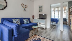 Ein Wohnzimmer mit einem blauen Sofa, einem Fernseher und einem kleinen runden Tisch.