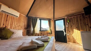 Een houten kamer met een bed, een klein tafeltje met handdoeken, een raam en een deur.
