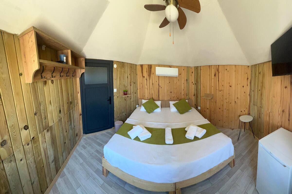 Una habitación con una cama, una mesita, un televisor y una puerta.