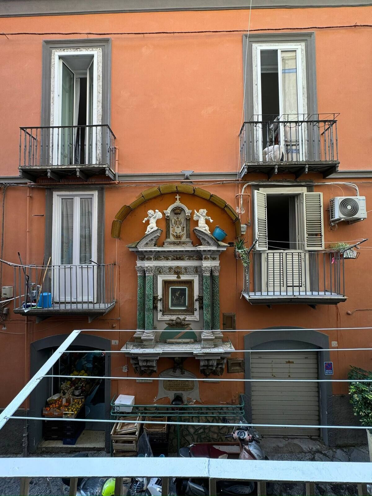A building with two balconies, a central decorative niche, and a garage door.