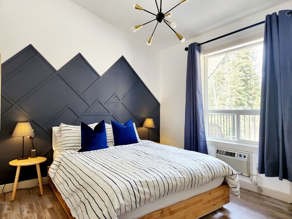 Une chambre à coucher moderne avec un lit, deux lampes de chevet, un luminaire au plafond et une fenêtre avec des rideaux.