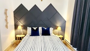 Een bed met gestreepte lakens, twee bedlampen, een donker hoofdbord, en een raam met gordijnen.
