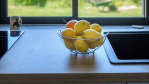 A kitchen counter with a fruit bowl containing lemons and an orange, and a window with a view of greenery and trees. - Rena Bianca, 25 m2, 6 min walk to the beach! (Coggia)